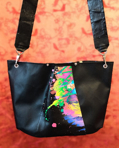 Vue arrière du sac Capri en simili cuir. Au centre, bande triangulaire multicolore. A gauche et à droite simili cuir noir. En haut du sac, deux boutons de col nickel sont vissés de chaque côtés de la partie multicolore. L'anse est en simili cuir noir et attachée au sac via des œillets et des mousquetons nickel.