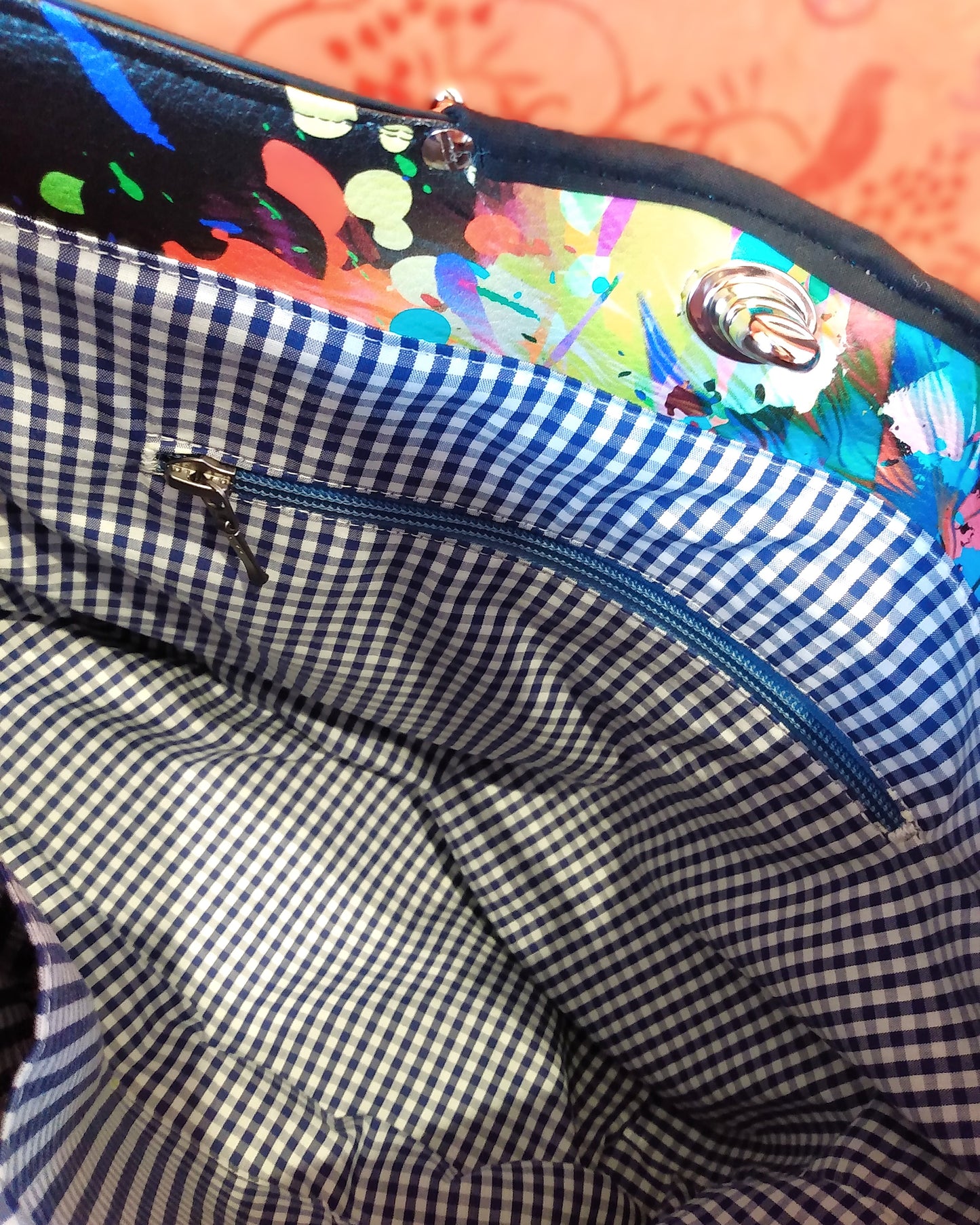 Vue intérieure du sac Capri. Doublure en coton à petits carreaux bleus et blancs. On voit une poche zippée dont la fermeture est bleue clair.
