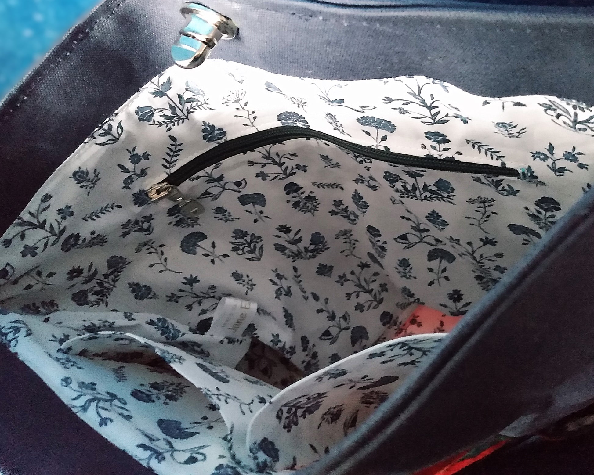 Intérieur du sac capri fleuri. Le tissu doublure est un coton blanc avec des fleurs bleu roi. On voit une poche zippée à fermeture éclair bleue. Deux poches plaquées sont également présentes.