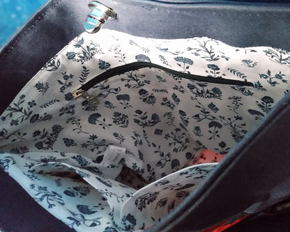 Intérieur du sac capri fleuri. Le tissu doublure est un coton blanc avec des fleurs bleu roi. On voit une poche zippée à fermeture éclair bleue. Deux poches plaquées sont également présentes.