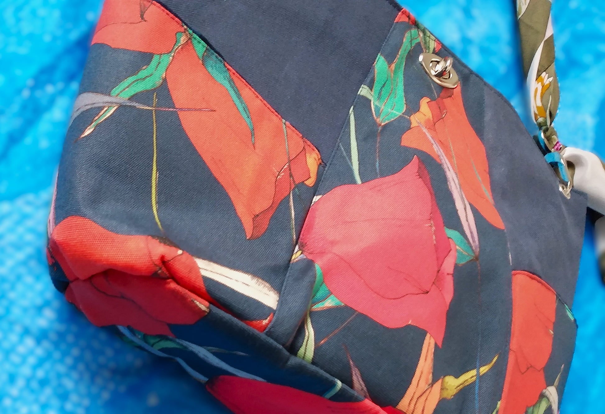 Vue du dessous sac capri fleuri. Le dessous du sac est en tissu déperlant avec imprimé gros coquelicots rouges et feuilles vertes sur fond bleu foncé.