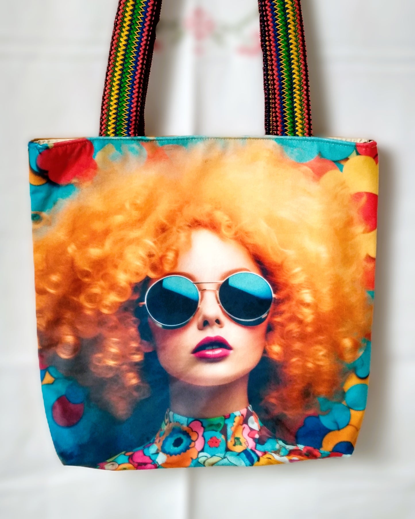Avant du sac Ginger. Velours imprimé tête de femme avec chevelure rousse et lunettes de soleil rondes. Le fond est à fleurs multicolores. Les anses sont multicolores.