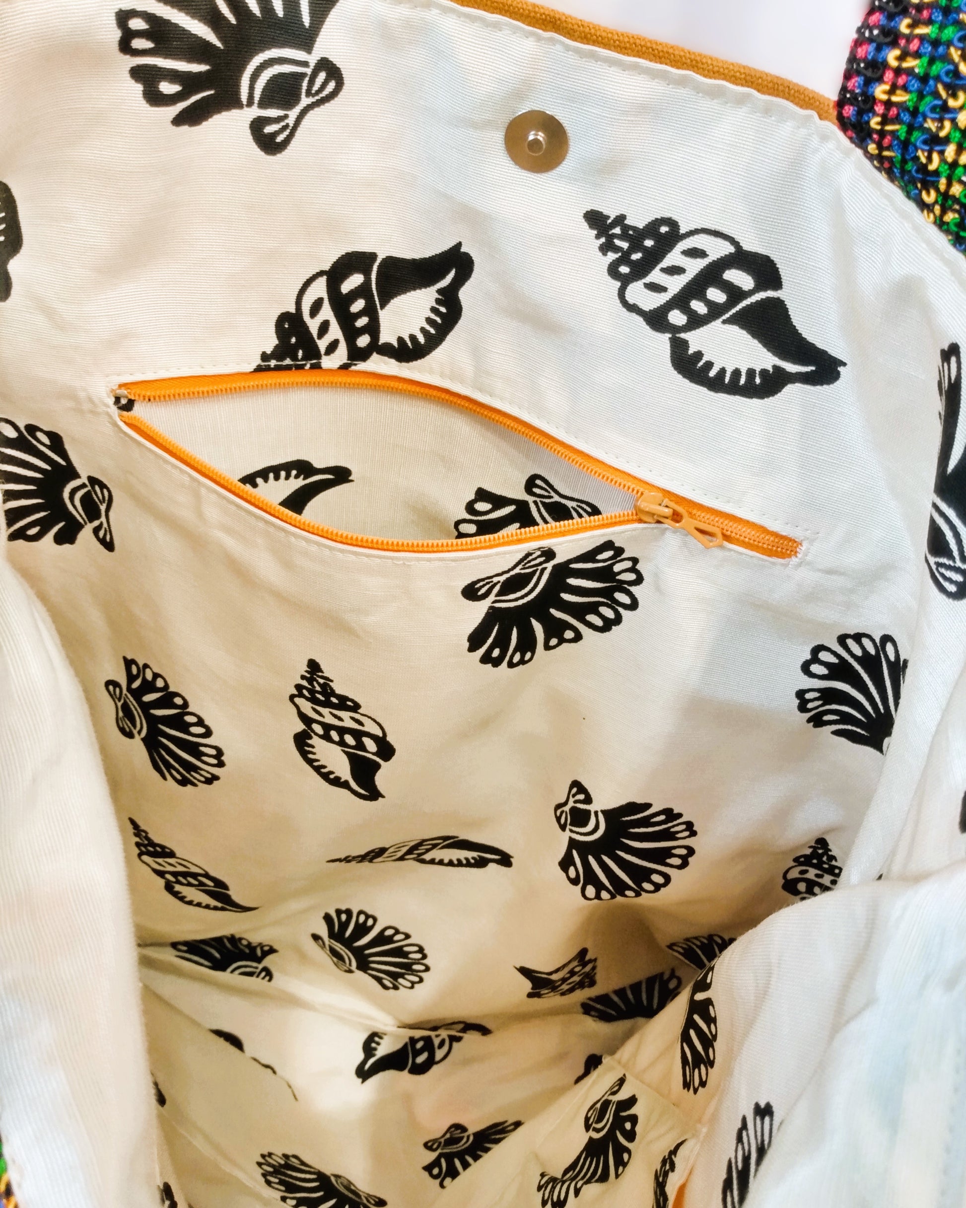 Intérieur du sac Ginger. Le tissu de doublure est beige avec de gros coquillages noirs. On voit une poche ouverte à fermeture orange et un fermoir aimanté pour fermer le sac.