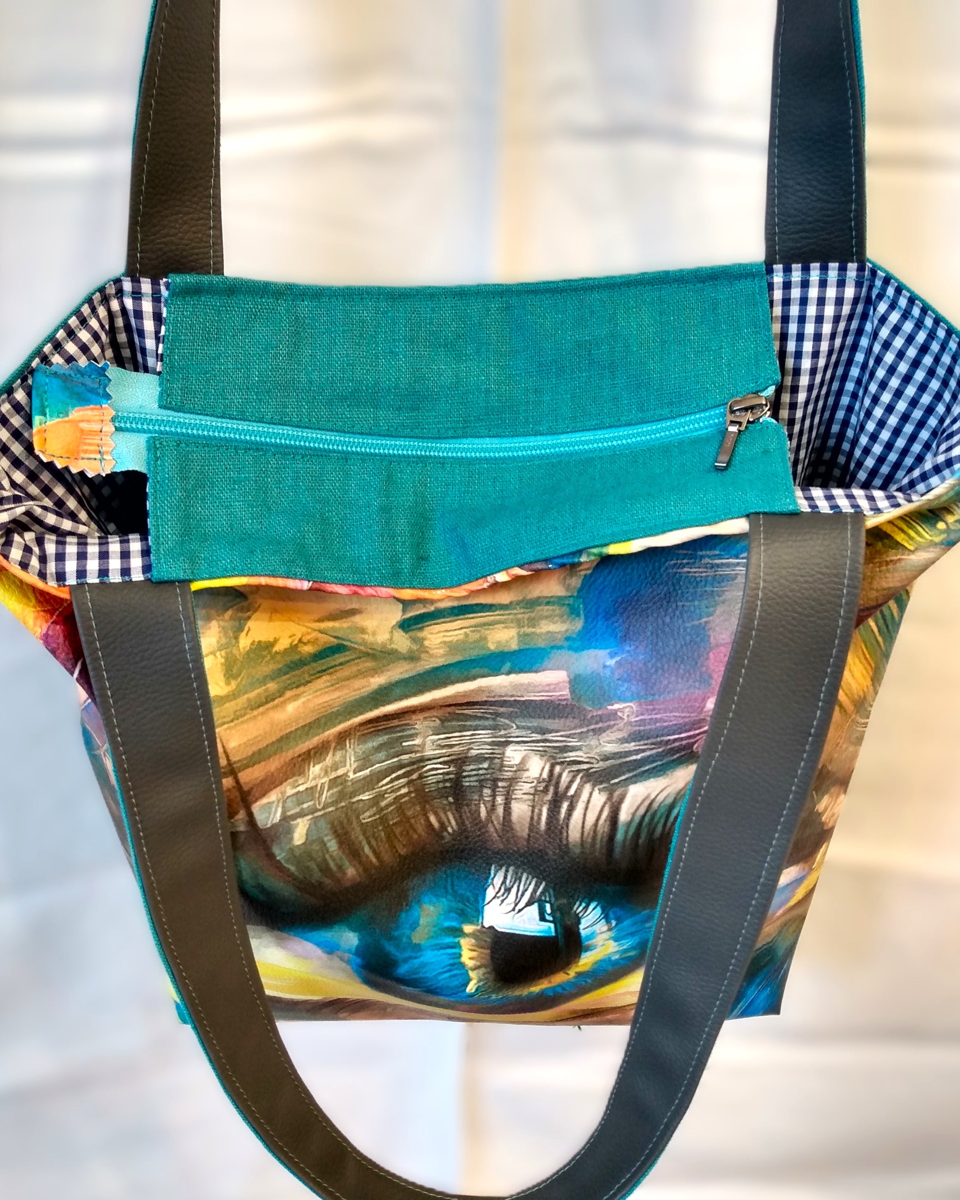 Dessus du sac Iris. Une fermeture éclair bleu ciel ferme le sac. On aperçoit la doublure en coton à petits carreaux bleus et blancs.