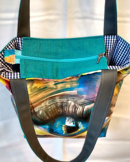 Dessus du sac Iris. Une fermeture éclair bleu ciel ferme le sac. On aperçoit la doublure en coton à petits carreaux bleus et blancs.