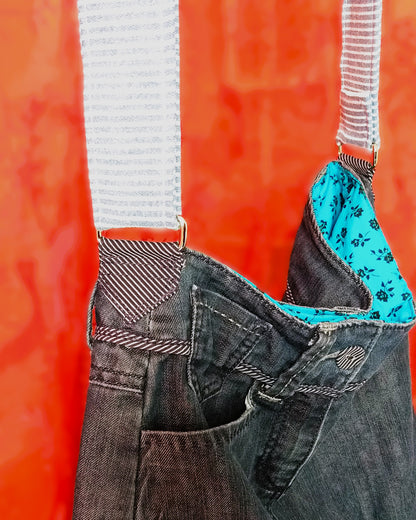 Vue latérale du sac Bleuet. L'extérieur correspond au haut d'un jean. Le jean est bleu/gris. La doublure est en coton bleu ciel à petites roses noires. La sangle réglable en jean à rayures blanches et bleues, est attachée au sac via un anneau rectangulaire.