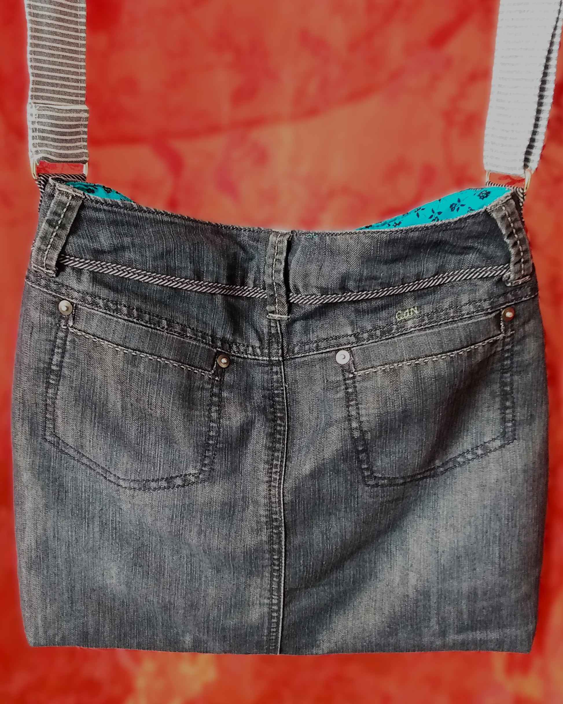 Vue arrière du sac Bleuet. L'extérieur correspond au haut d'un jean, avec deux poches arrières. Le jean est bleu/gris. La doublure est en coton bleu ciel à petites roses noires. La sangle réglable est en jean à rayures bleues et blanches.