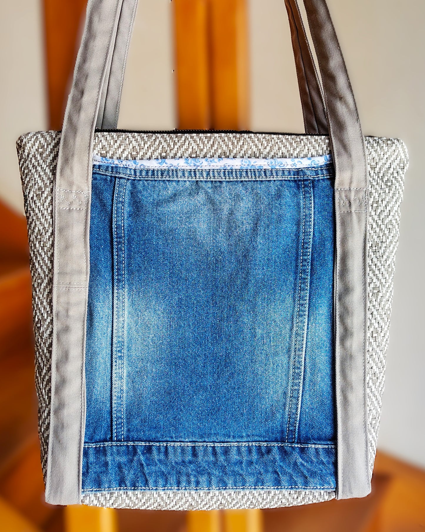 Arrière du sac OriJean. tissu principal en simili cuir motif tissage gris et blanc. Grande poche arrière fabriquée à partir de l'arrière d'une veste en jean bleue. Les anses sont en coton gris clair. Le sac se ferme avec une fermeture éclair métal.