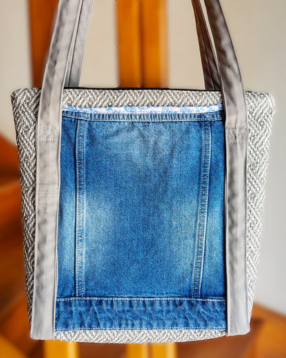 Arrière du sac OriJean. tissu principal en simili cuir motif tissage gris et blanc. Grande poche arrière fabriquée à partir de l'arrière d'une veste en jean bleue. Les anses sont en coton gris clair. Le sac se ferme avec une fermeture éclair métal.