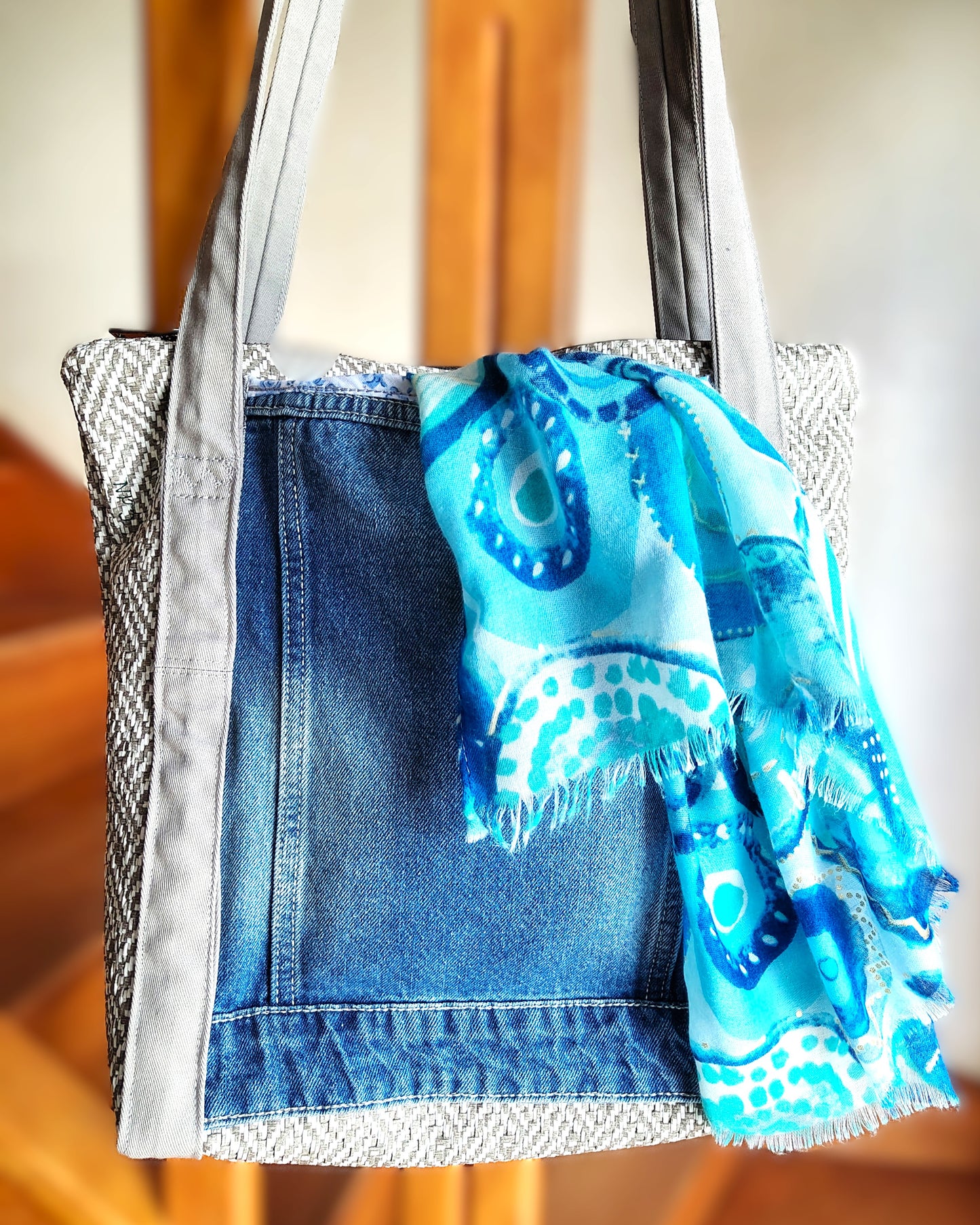 Arrière du sac OriJean. tissu principal en simili cuir motif tissage gris et blanc. Grande poche arrière fabriquée à partir de l'arrière d'une veste en jean bleue. Les anses sont en coton gris clair. Le sac se ferme avec une fermeture éclair métal.