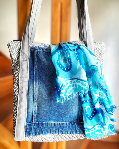 Arrière du sac OriJean. tissu principal en simili cuir motif tissage gris et blanc. Grande poche arrière fabriquée à partir de l'arrière d'une veste en jean bleue. Les anses sont en coton gris clair. Le sac se ferme avec une fermeture éclair métal.