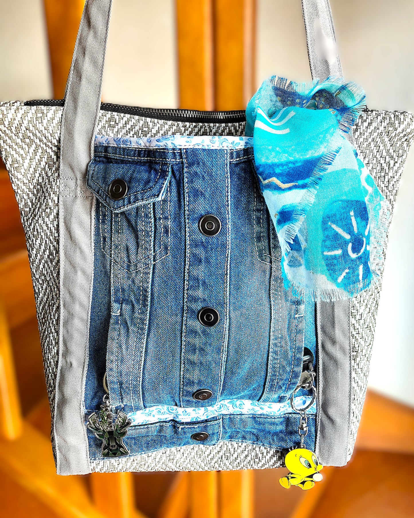 Avant du sac OriJean. tissu principal en simili cuir motif tissage gris et blanc. Grande poche avant fabriquée à partir de l'avant d'une veste en jean. Les anses sont en coton gris clair. Le sac se ferme avec une fermeture éclair métal.
