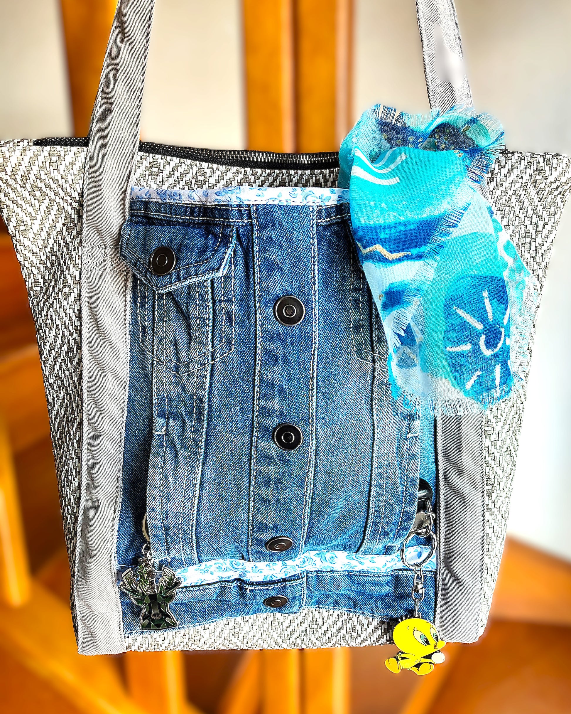Avant du sac OriJean. tissu principal en simili cuir motif tissage gris et blanc. Grande poche avant fabriquée à partir de l'avant d'une veste en jean. Les anses sont en coton gris clair. Le sac se ferme avec une fermeture éclair métal.