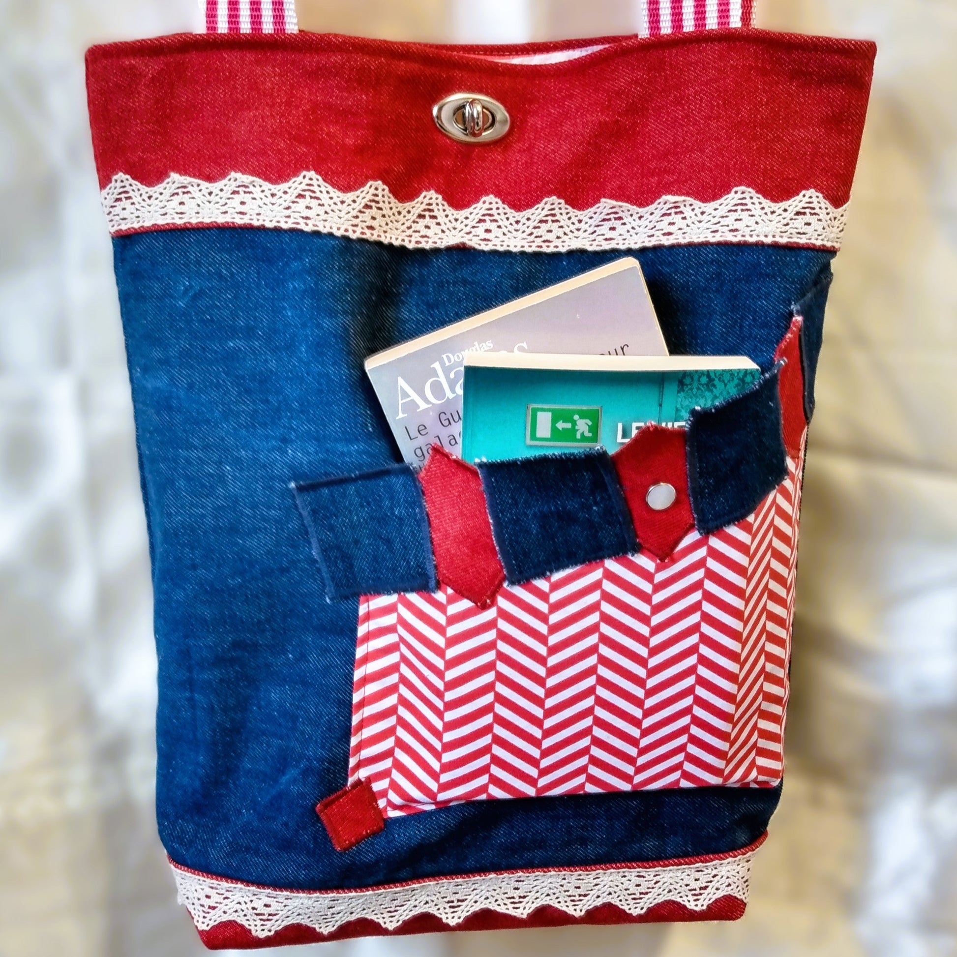 avant du sac Boujou. Couleurs principales, bleu, rouge et blanc. Extérieur en jean denim. Voir description détaillée sur la photo précédente. Seule différence avec l'autre photo, ici la poche avant contient deux livres de poche.