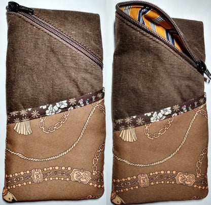 Étui à lunettes velours marron. Se ferme avec un zip marron. A l'extérieur, une poche marron plus clair à motifs chaînettes, surmontée d'un biais marron à fleurs est visible à l'avant, sur la moitié basse de l'étui. L'intérieur est à rayures orange et bleu marine.
