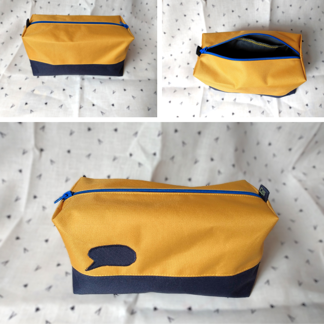 Trois vues de la trousse corail bleu foncé et jaune. 1) vue de l'arrière de la trousse bicolore ligne jaune moutarde en haut et ligne bleu foncé en bas. Se ferme avec une fermeture éclair bleu roi. 2) vue de l'intérieur de la trousse. La doublure est en coton gris anthracite et une poche plaquée grise avec un liseré jaune est visible. 3) avant extérieur de la trousse où l'on voit la bulle de BD. Voir photo précédente pour plus de précision.