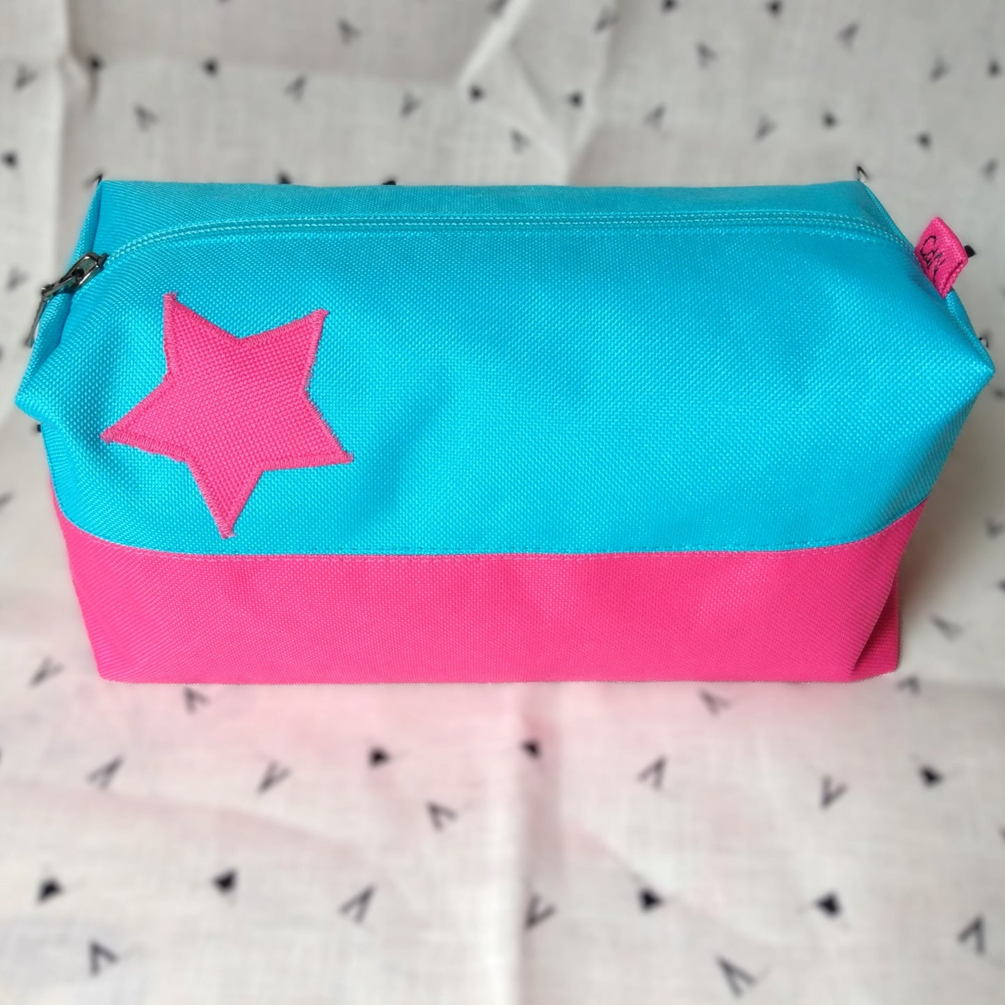Trousse de toilette Corail rectangulaire et bicolore, en horizontal. Rose en bas et bleu ciel en haut. Un appliqué rose en forme d'étoile est présent sur la rayure bleue. Elle se ferme avec une fermeture éclair bleu ciel.