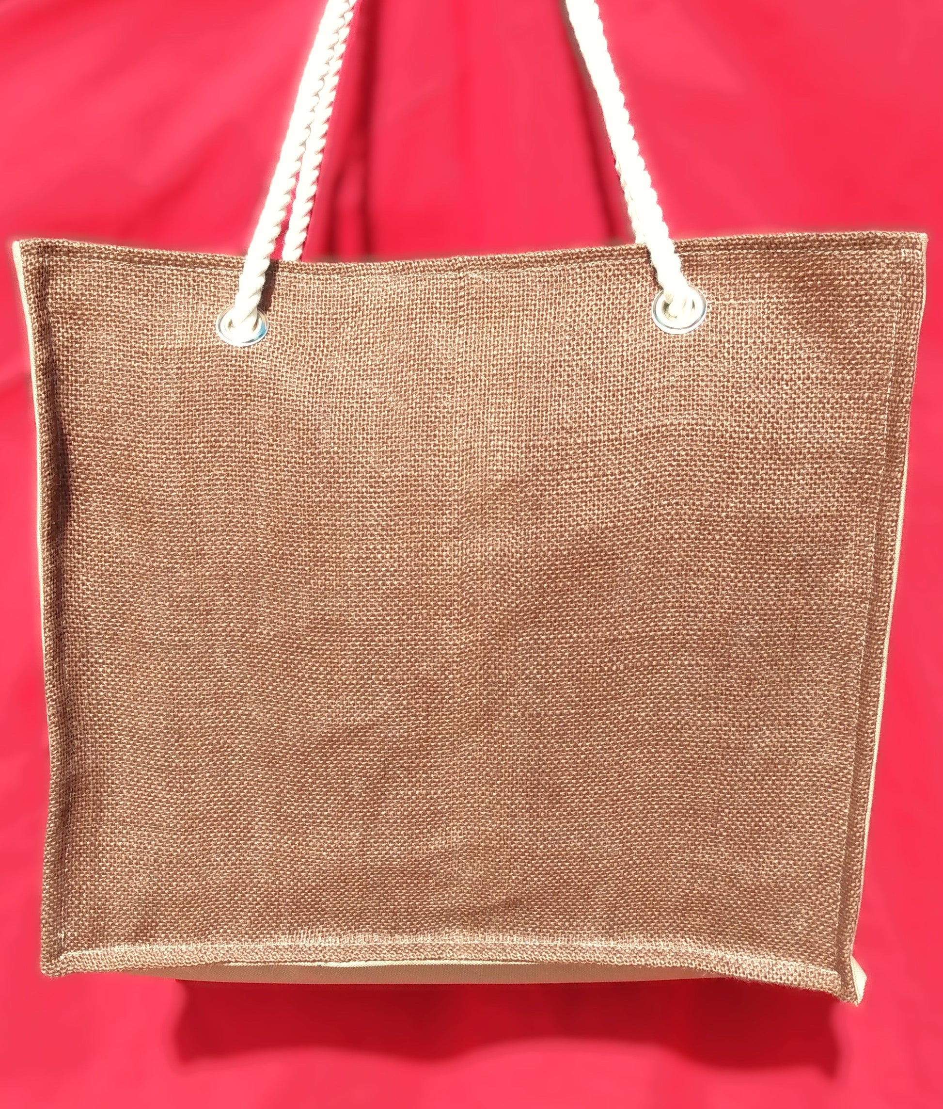 Avant et arrière du sac Peinard. Sac en toile de jute marron, de forme carrée. Les anses sont en corde blanche. Les anses sont accrochées via des œillets en métal nickelé. Le fond de l'image est rouge.