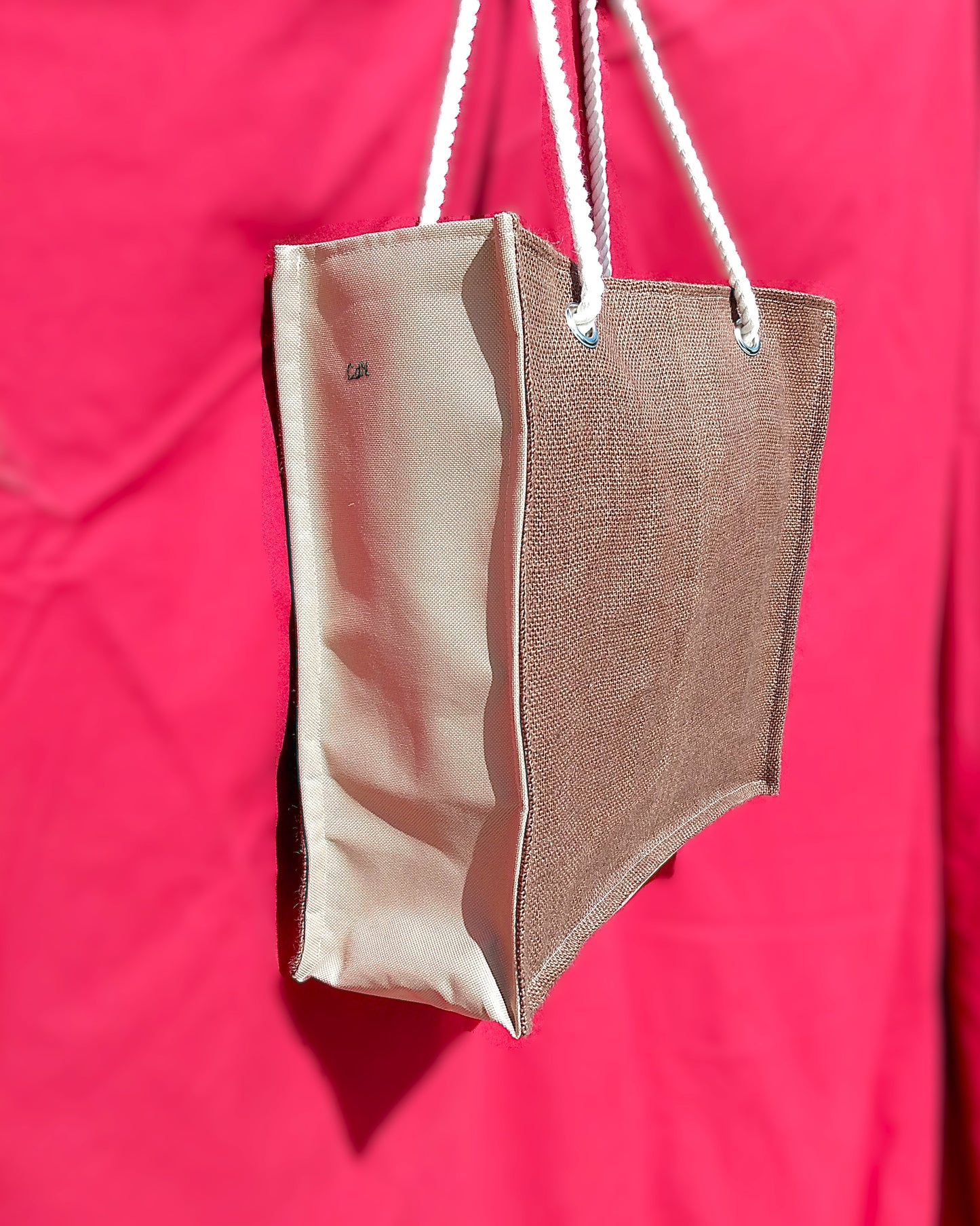 Sac Peinard vu de côté. L'avant du sac est en toile de jute marron. Les côtés du sac sont en toile à sac imperméable beige. Les anses sont en corde. Le sac est de forme rectangulaire.