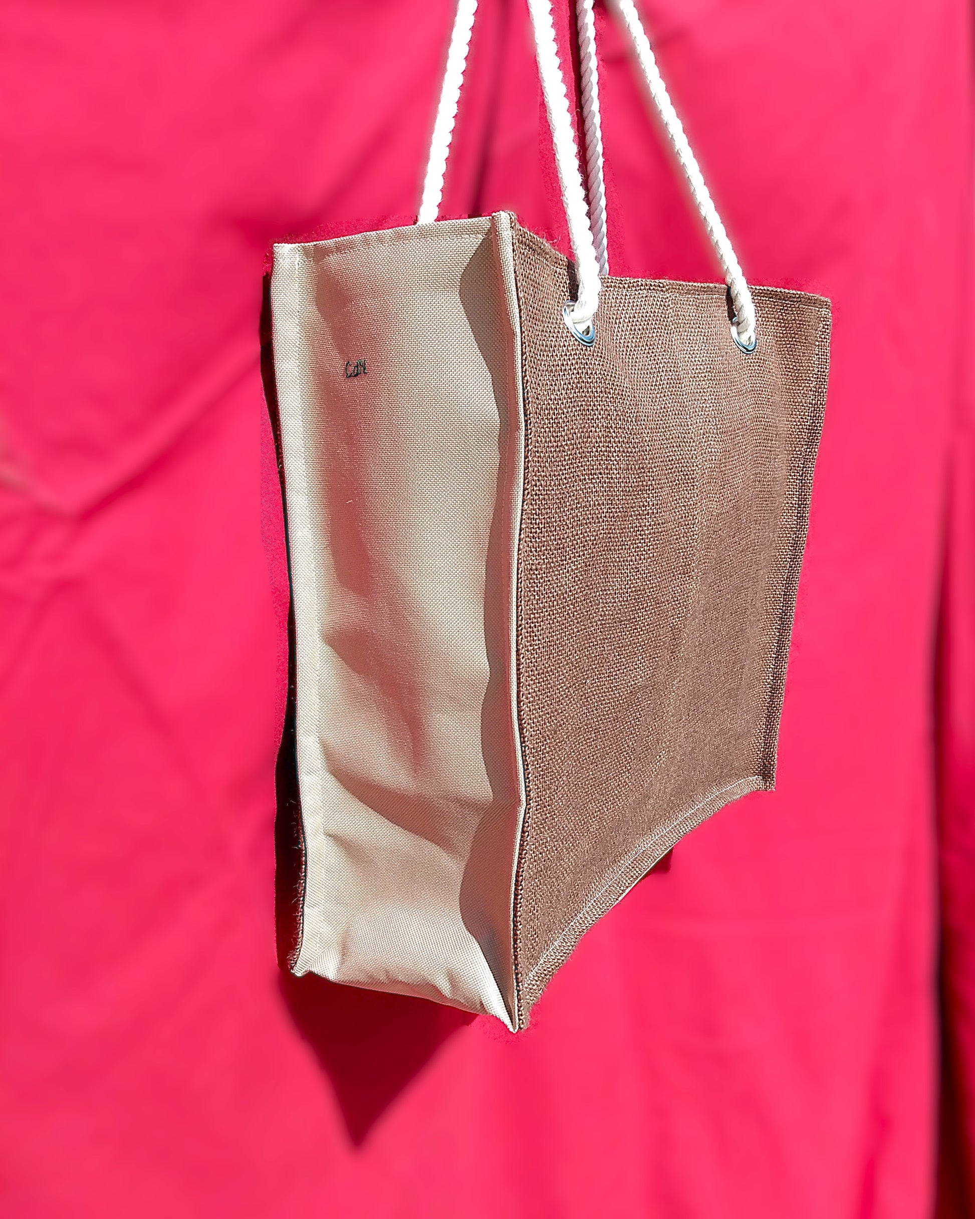 Sac Peinard vu de côté. L'avant du sac est en toile de jute marron. Les côtés du sac sont en toile à sac imperméable beige. Les anses sont en corde. Le sac est de forme rectangulaire.